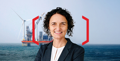 Satya pictured smiling at the camera in front of a background of an oversea wind turbine